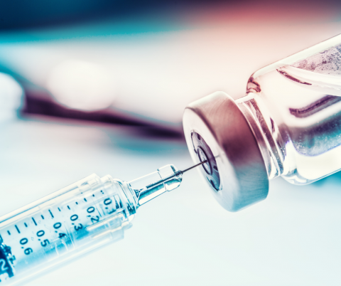 A needle pierces a vial of vaccine.